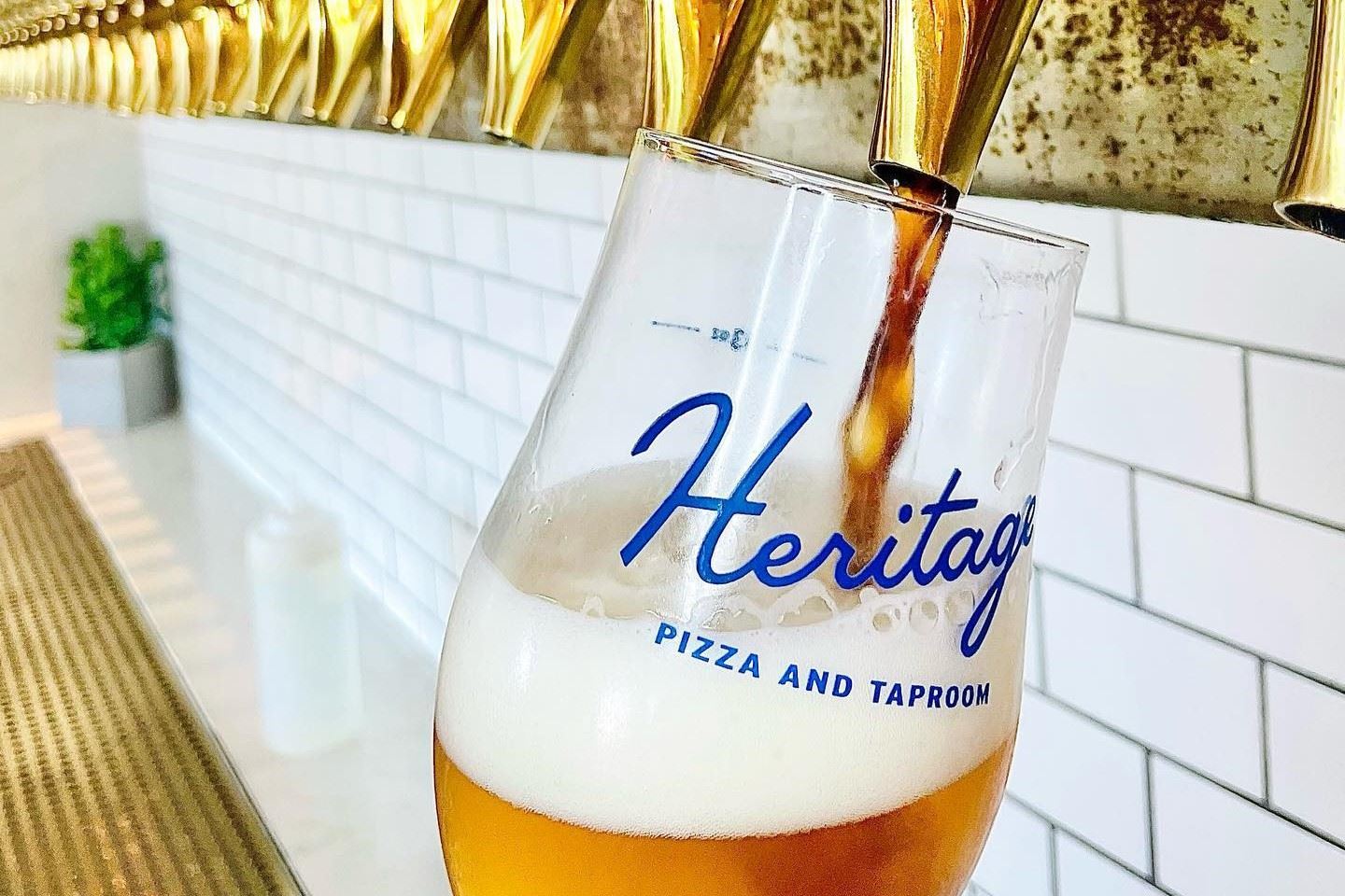 Beer being poured into a Heritage Pizza and Taproom glass from a golden tap