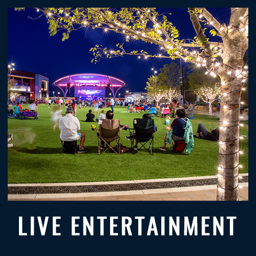 People sit on lawn chairs at night watching a live outdoor concert under a lit stage