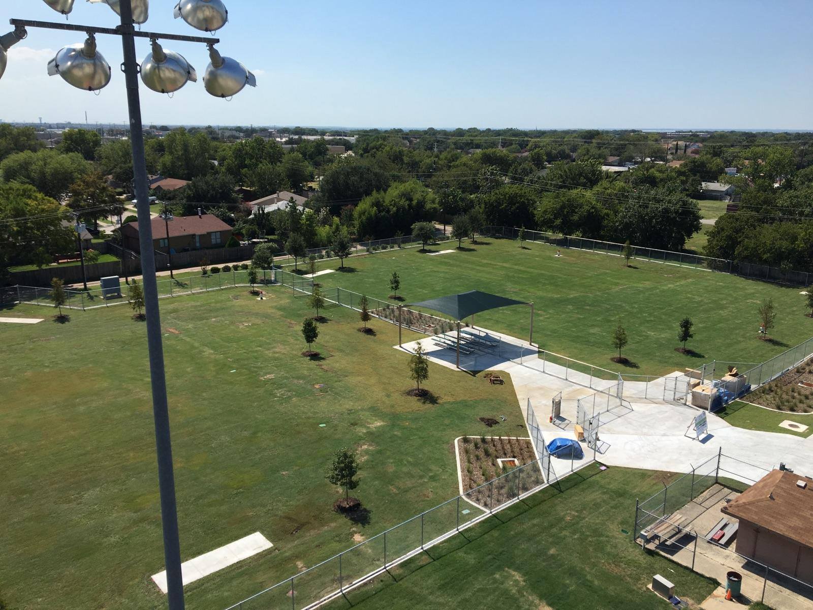 Aerial view of a large green dog park with shade structure, paths and fenced areas.