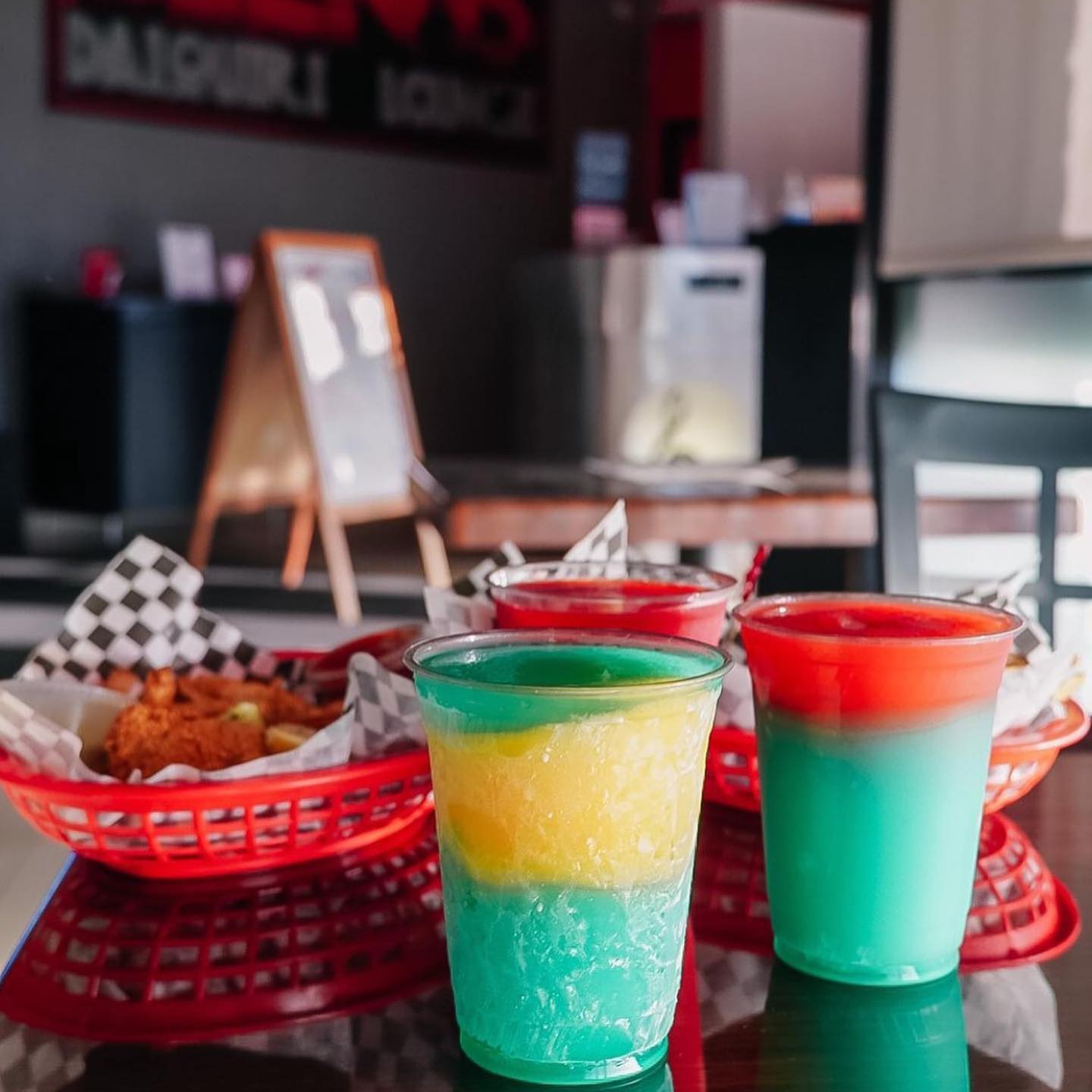 Colorful frozen drinks and fried food baskets on a table at a casual daiquiri lounge.