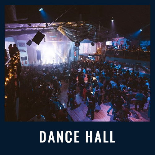 Crowded dance hall with people dancing under blue lights and a large disco ball overhead.