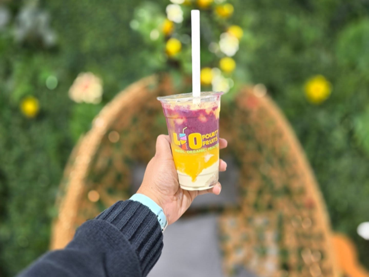 Hand holding a colorful fruit smoothie from 40 Fruits with a garden background.