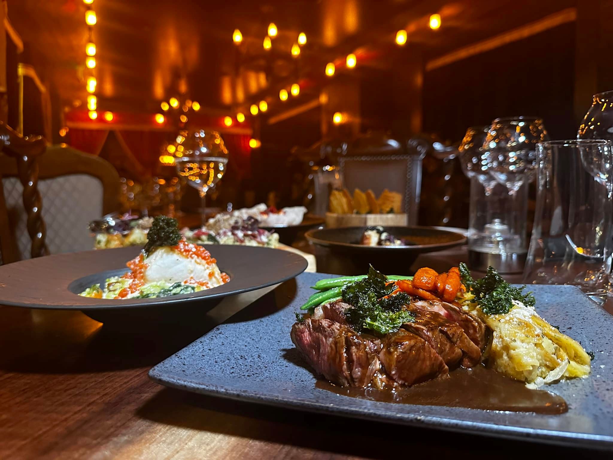 Gourmet steak dinner and plated appetizer in an elegant, dimly lit fine dining restaurant.