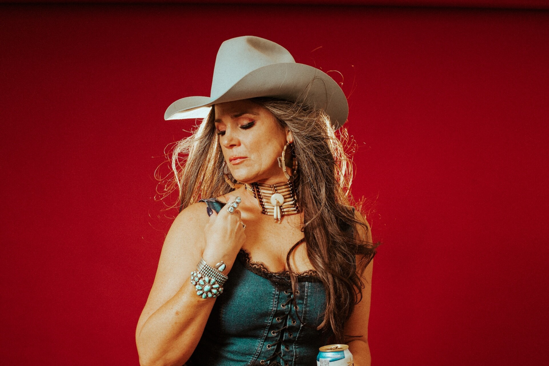 Woman in a cowboy hat and turquoise jewelry poses against a red background.