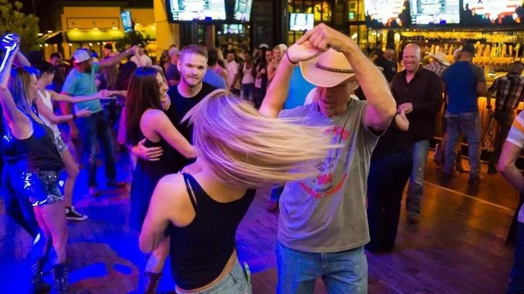 People dancing in a lively bar with colorful lights, cowboy hats and a packed, energetic atmosphere